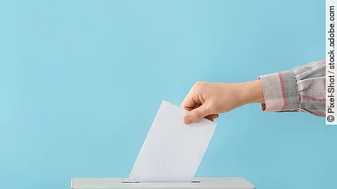 Wahl Ein Wahlzettel wird in eine graue Wahlurne geschmissen.